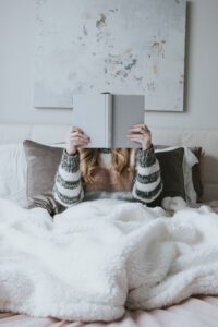 personne féminine lisant un livre sous un plaid avec coussin